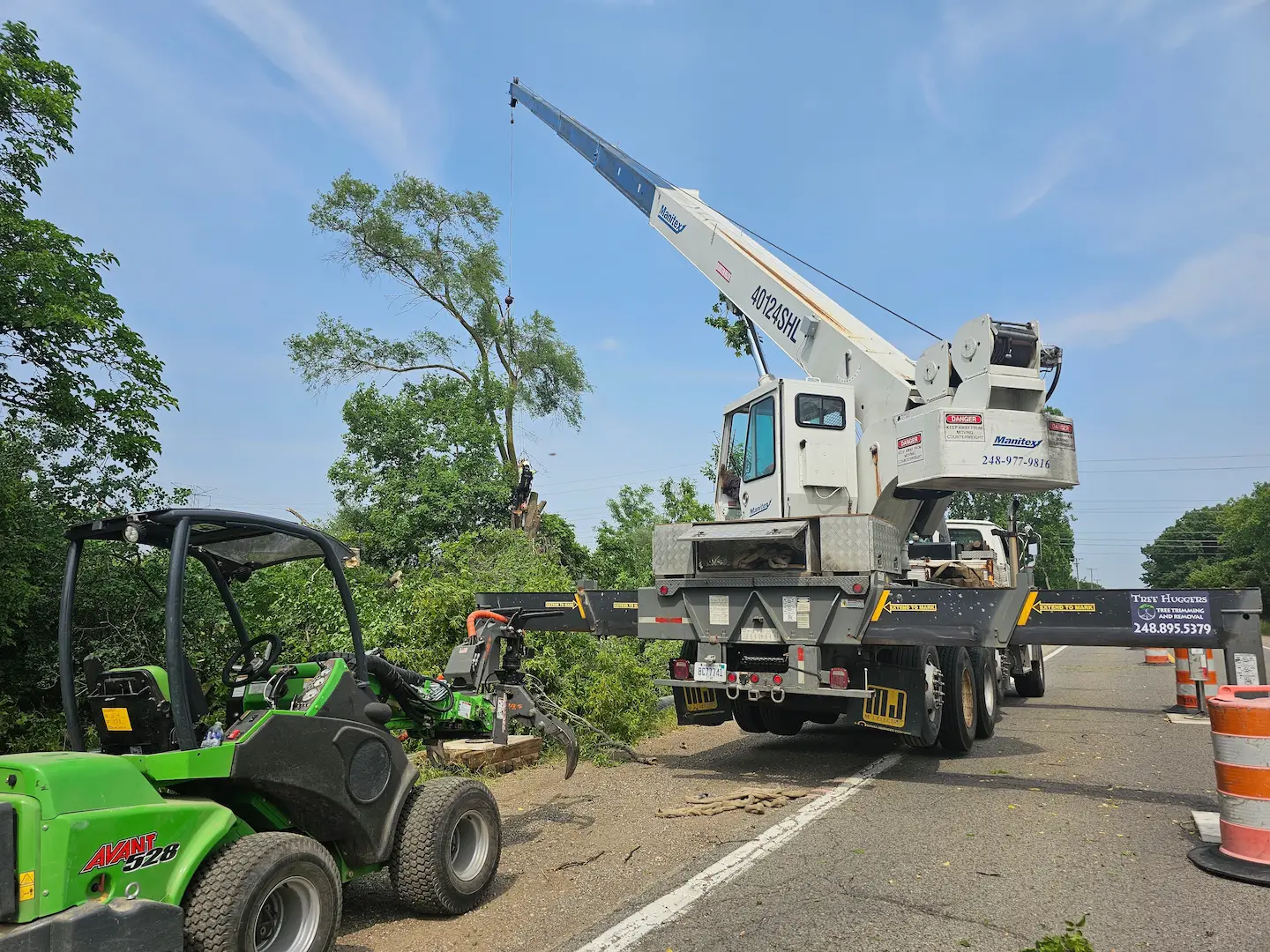 Crane and Bobcat removing tree branches near a road.