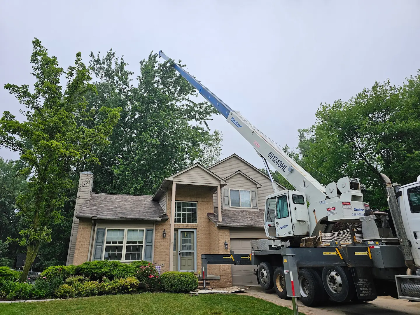 Manitex 40124SHL crane removing tree branches near a house.